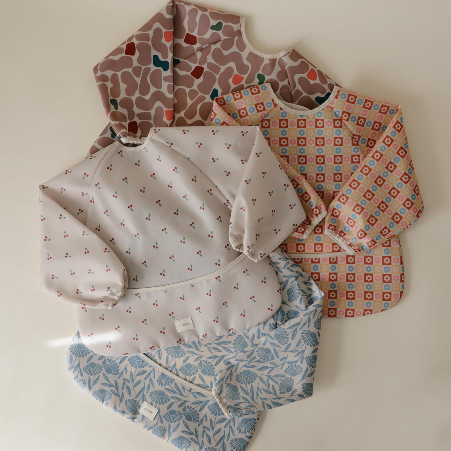 mushie Long Sleeve Baby Bib | Water Resistant Adjustable Fit for Ages 6-24 Months (Happy Flowers Check)